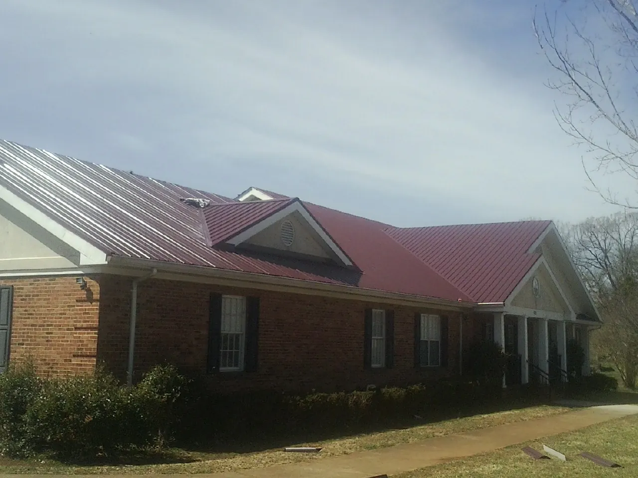 Red metal roof with gabled entries on a long brick building, from a Hail Damage Roof Repair job in Minersville