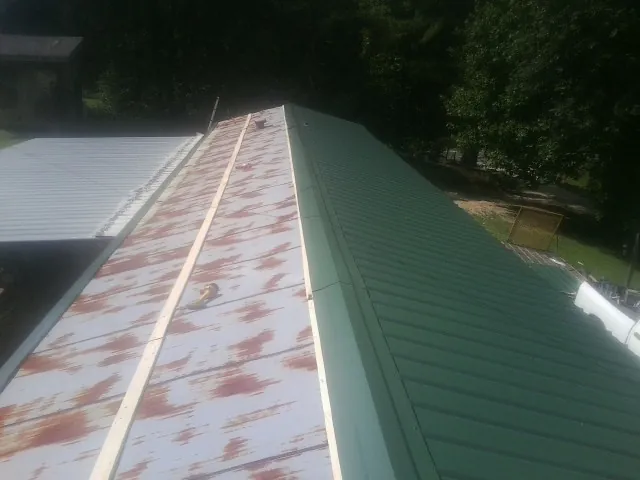 Old rusted panels beside newly installed green metal roofing — Wind Damage Roof Repair by Roofing Brothers in Minersville