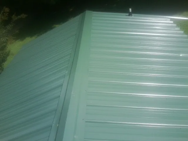 New green metal panels meeting at the ridge of a roof — Flat Roof Repair work by our crew in Minersville