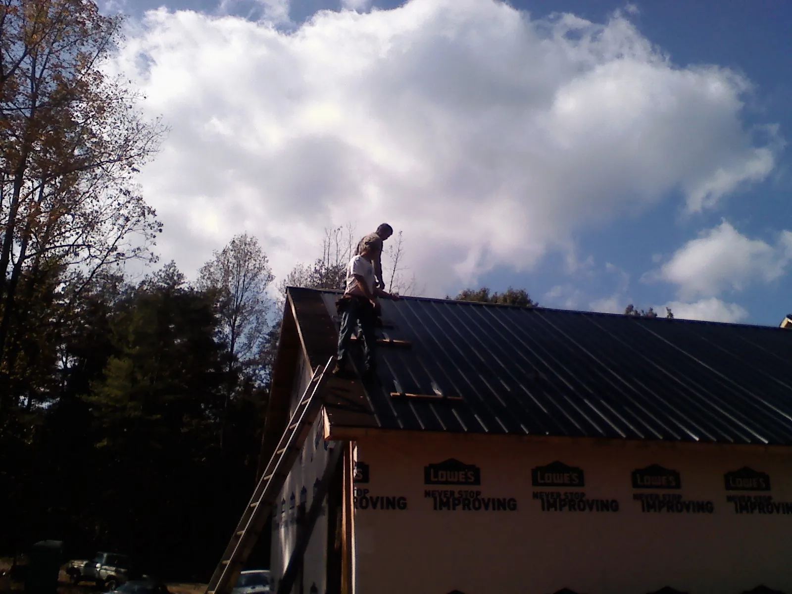 Roofer fastening dark metal panels high against a cloudy sky, from a Roof Inspection job in Minersville